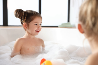 Photo of Cute little girl taking bubble bath at home