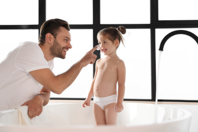 Photo of Young father with cute little daughter in bathroom