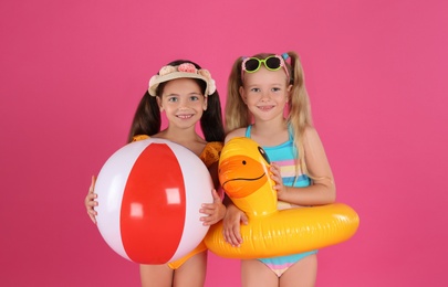 Cute little children in beachwear with bright inflatable toys on pink background Photo of Cute little children in beachwear with bright inflatable toys on pink background