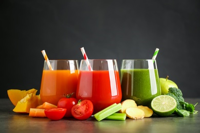 Different tasty juices and fresh ingredients on grey table against black background Photo of Different tasty juices and fresh ingredients on grey table against black background