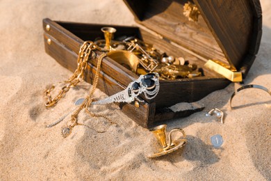 Open wooden chest with treasures on sand Photo of Open wooden chest with treasures on sand