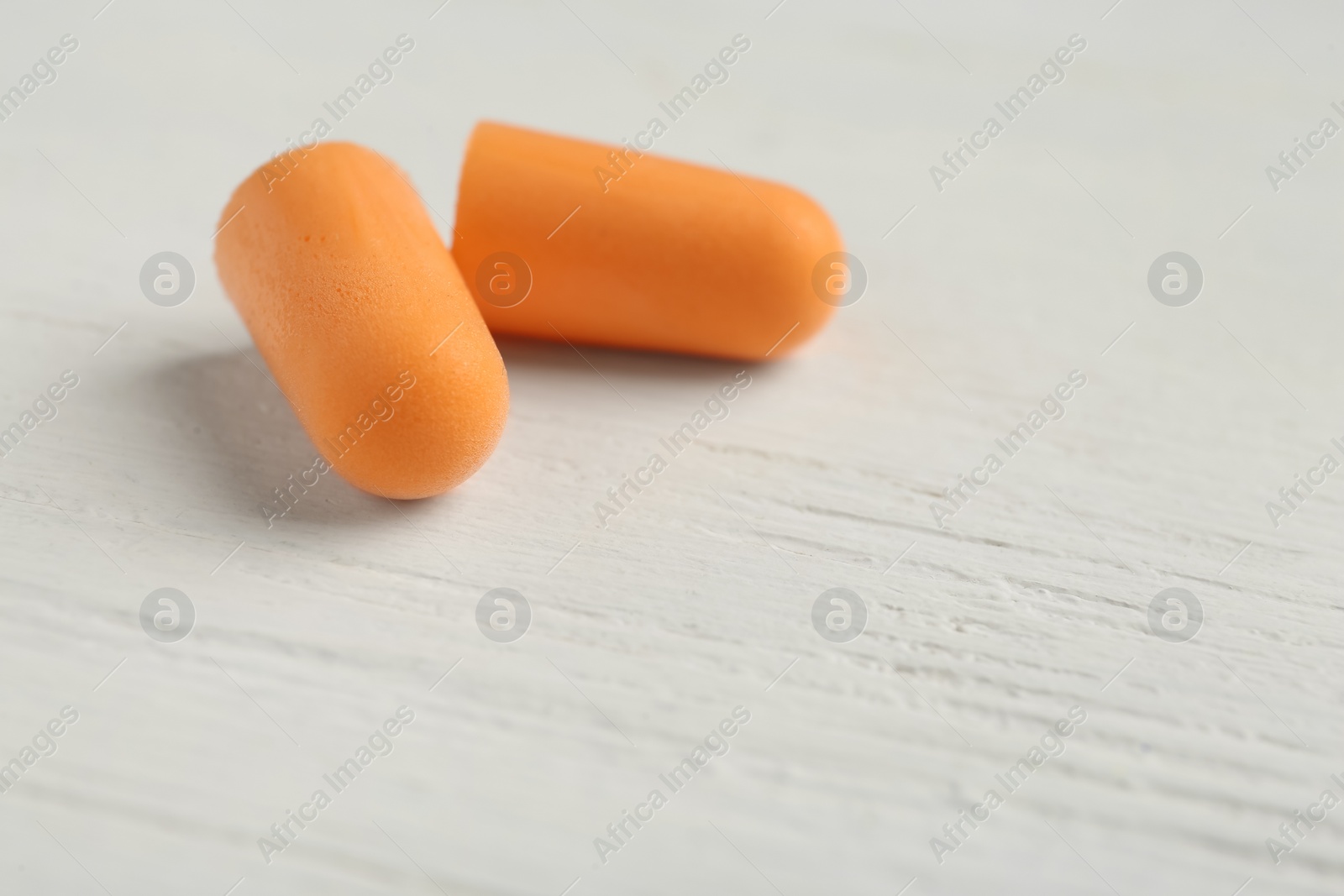 Pair of orange ear plugs on white wooden background, closeup. Space for text Photo of Pair of orange ear plugs on white wooden background, closeup. Space for text