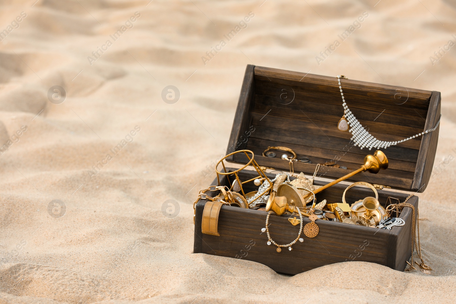 Open wooden treasure chest on sand, space for text Photo of Open wooden treasure chest on sand, space for text