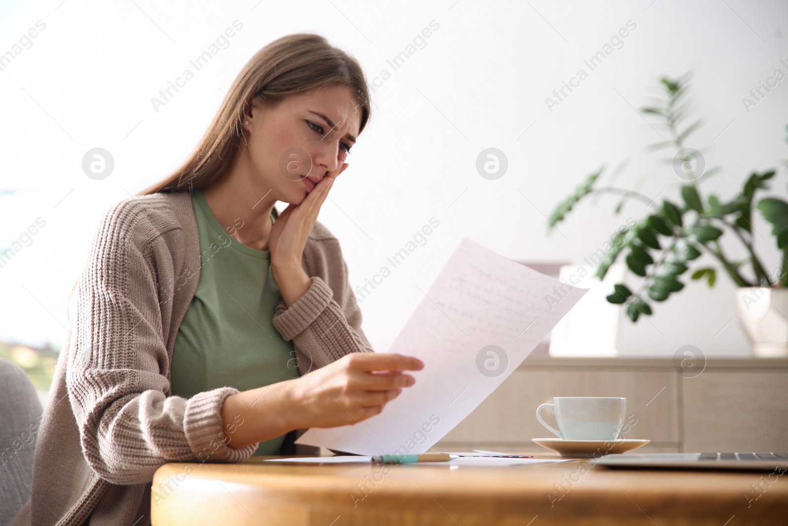 Worried woman reading letter at wooden table in room Photo of Worried woman reading letter at wooden table in room