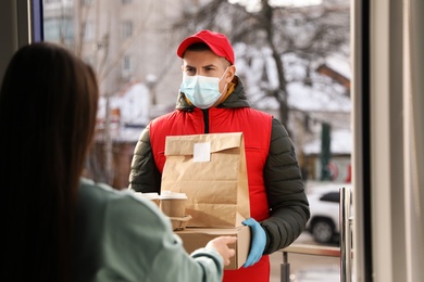 Courier in medical mask giving to woman her order at doorway. Delivery service during Covid-19 quarantine Photo of Courier in medical mask giving to woman her order at doorway. Delivery service during Covid-19 quarantine