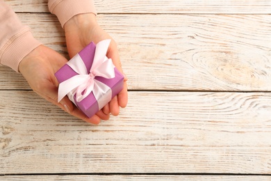 Photo of Woman holding gift box at white wooden table, above view with space for text. Valentine's Day celebration