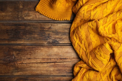 Photo of Orange knitted plaid on wooden table, top view. Space for text