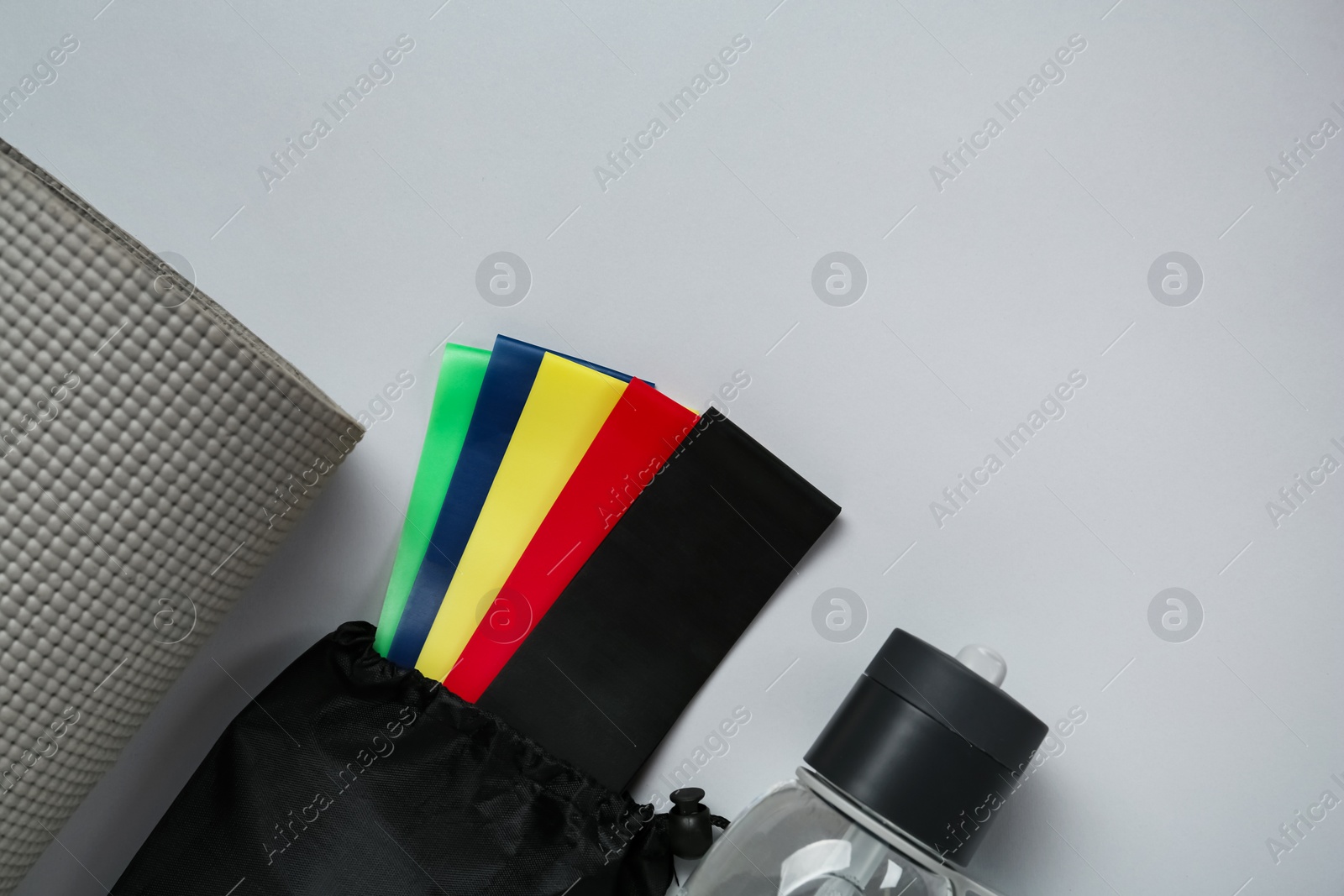Set of fitness elastic bands, yoga mat and water bottle on grey background, flat lay. Space for text Photo of Set of fitness elastic bands, yoga mat and water bottle on grey background, flat lay. Space for text