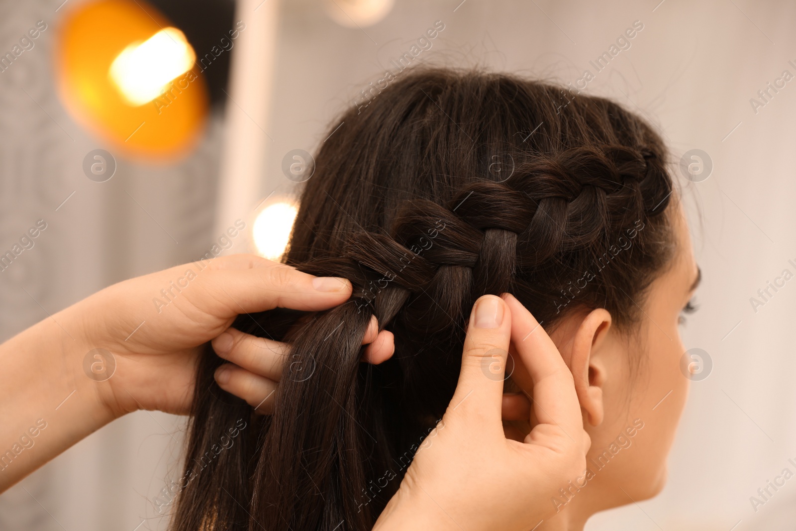 Professional stylist braiding client's hair on blurred background, closeup Photo of Professional stylist braiding client's hair on blurred background, closeup