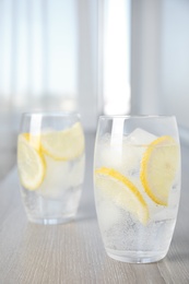 Soda water with lemon slices and ice cubes on wooden table indoors Photo of Soda water with lemon slices and ice cubes on wooden table indoors