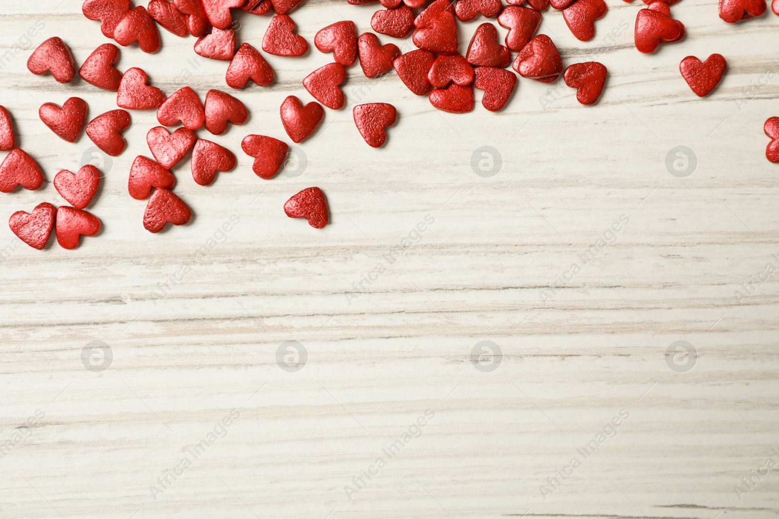 Bright heart shaped sprinkles on white wooden table, flat lay. Space for text Photo of Bright heart shaped sprinkles on white wooden table, flat lay. Space for text