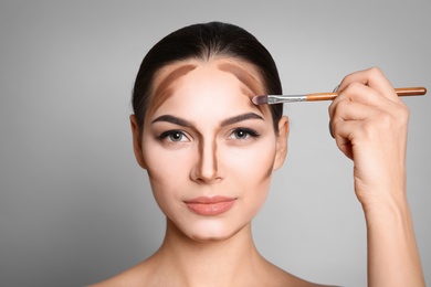 Young woman applying contouring lines on grey background. Professional makeup products Photo of Young woman applying contouring lines on grey background. Professional makeup products