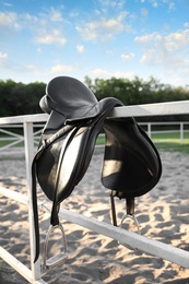 Leather horse saddle on wooden fence outdoors Photo of Leather horse saddle on wooden fence outdoors