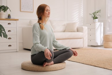 Photo of Woman meditating on wicker mat at home