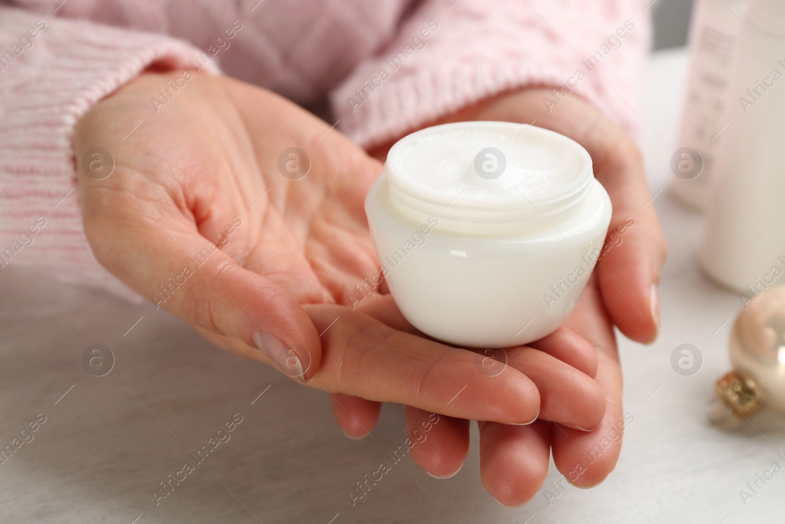 Woman holding jar of cream at light table, closeup. Cosmetic product for winter Photo of Woman holding jar of cream at light table, closeup. Cosmetic product for winter