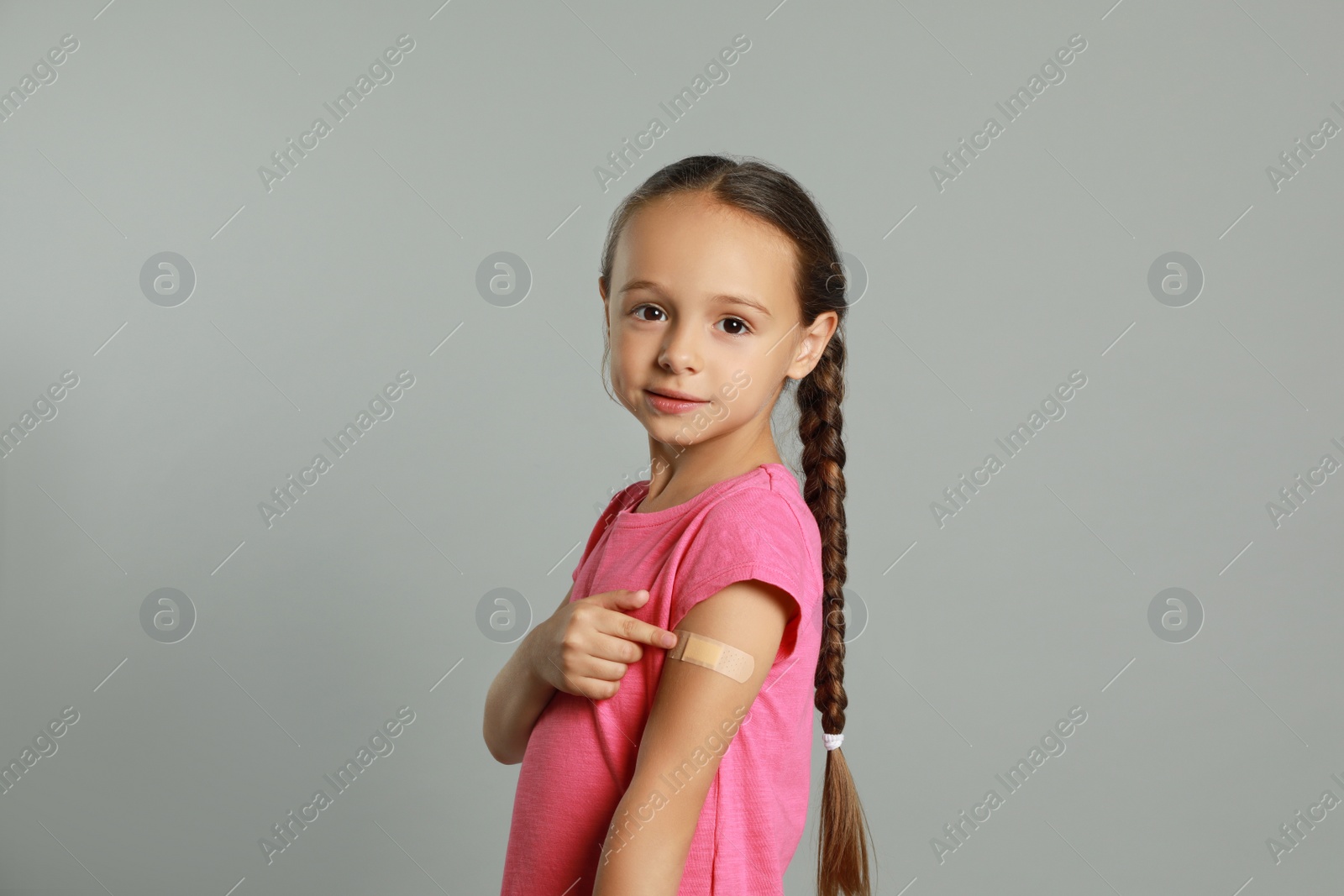 Vaccinated little girl showing medical plaster on her arm against light grey background Photo of Vaccinated little girl showing medical plaster on her arm against light grey background