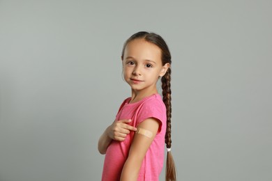 Vaccinated little girl showing medical plaster on her arm against light grey background Photo of Vaccinated little girl showing medical plaster on her arm against light grey background