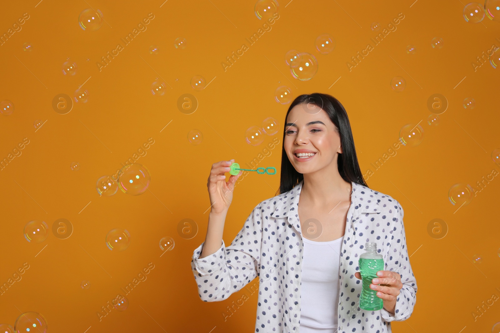 Young woman blowing soap bubbles on yellow background Photo of Young woman blowing soap bubbles on yellow background