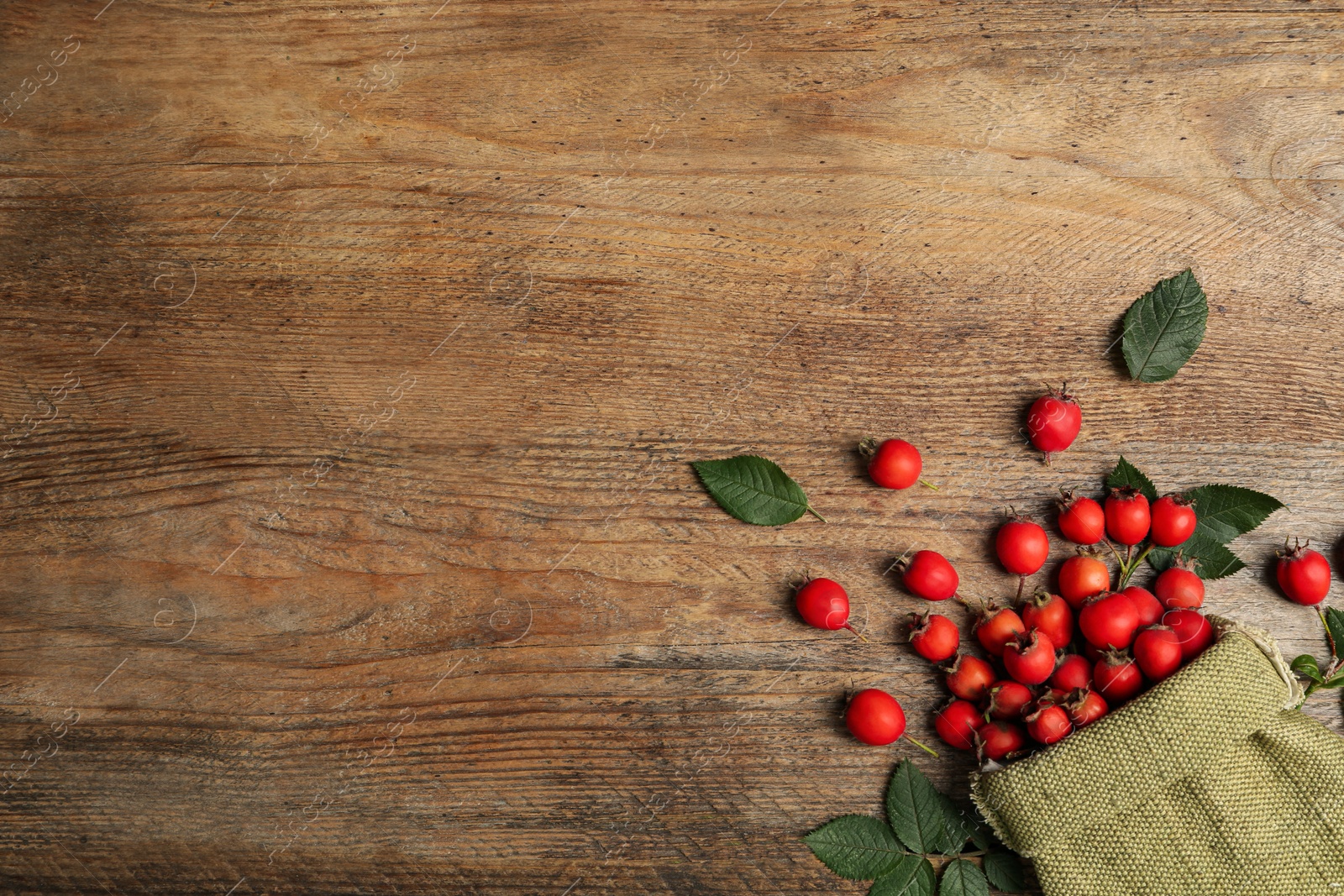 Ripe rose hip berries with green leaves on wooden table, flat lay. Space for text Photo of Ripe rose hip berries with green leaves on wooden table, flat lay. Space for text