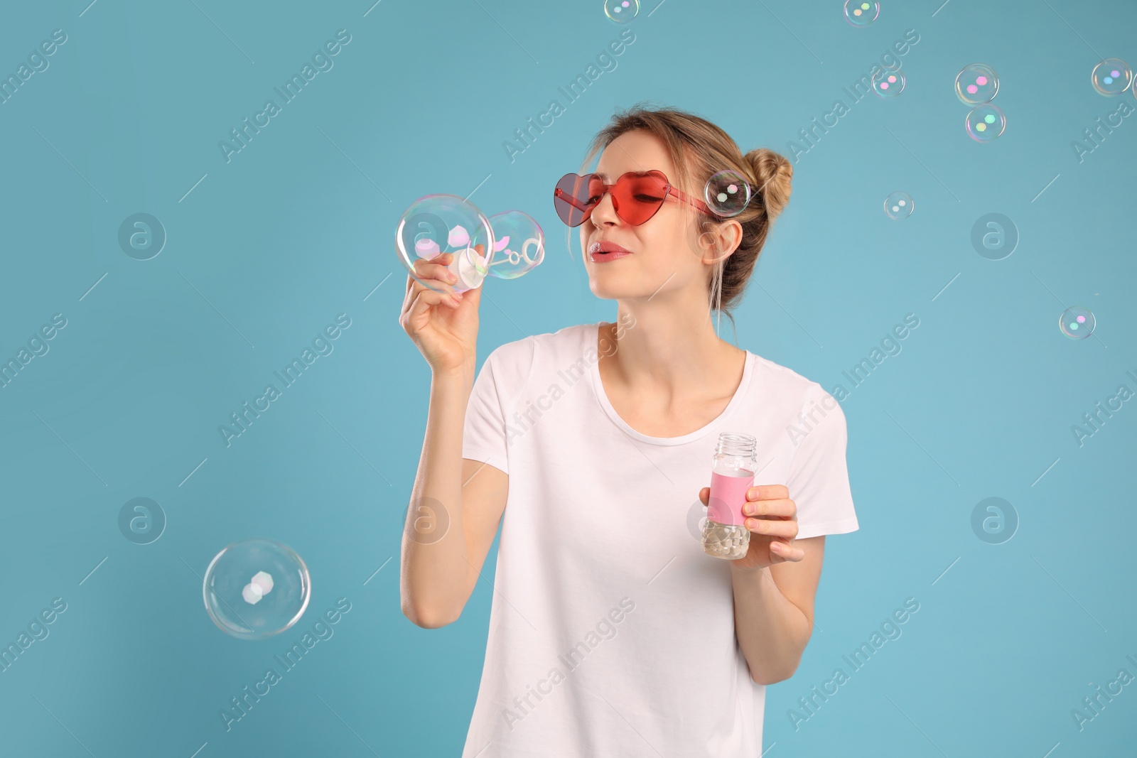 Young woman blowing soap bubbles on light blue background Photo of Young woman blowing soap bubbles on light blue background