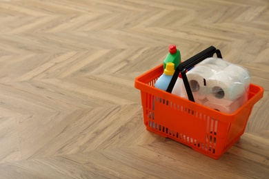 Photo of Shopping basket with household goods on wooden floor. Space for text