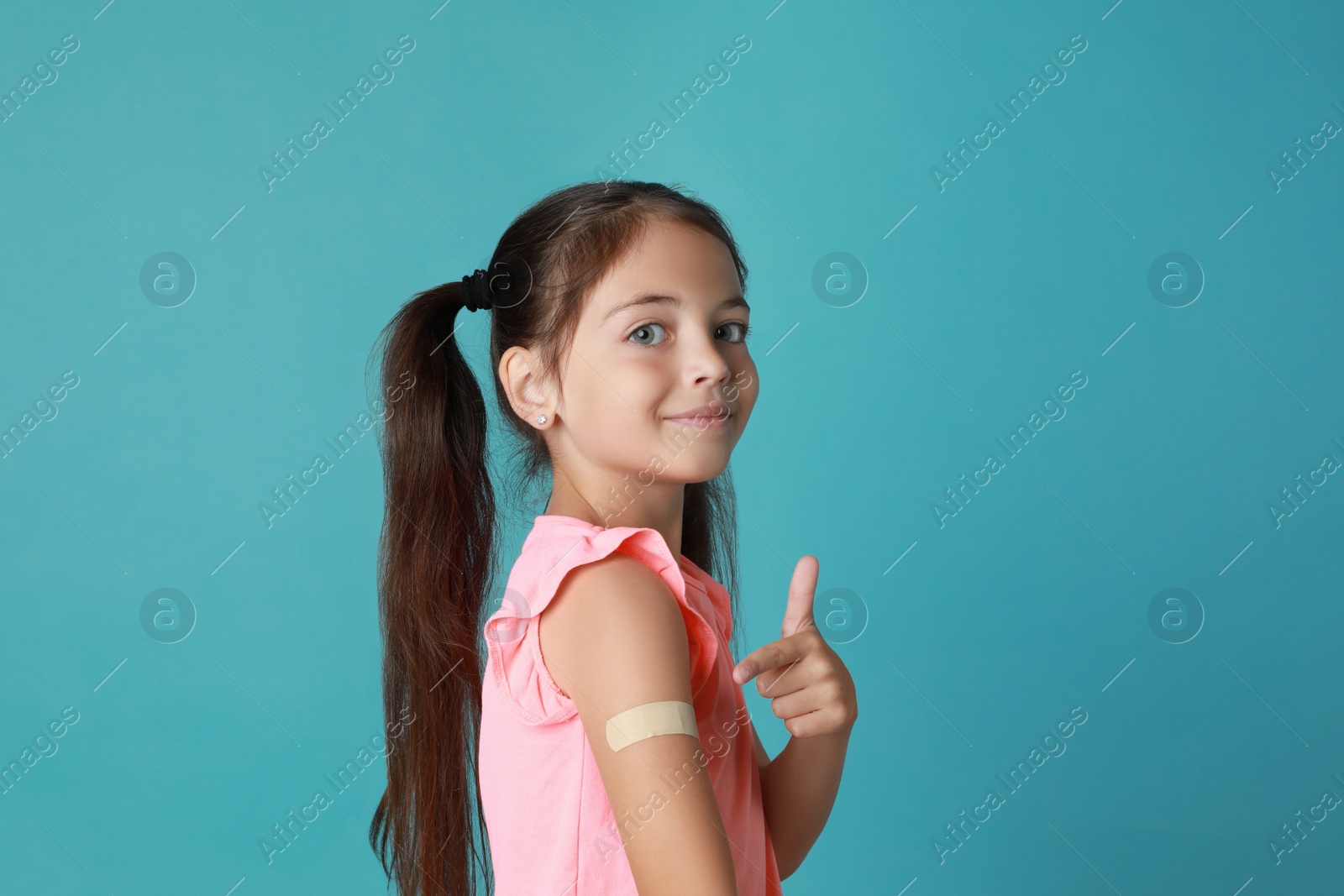 Vaccinated little girl showing medical plaster on her arm against light blue background Photo of Vaccinated little girl showing medical plaster on her arm against light blue background