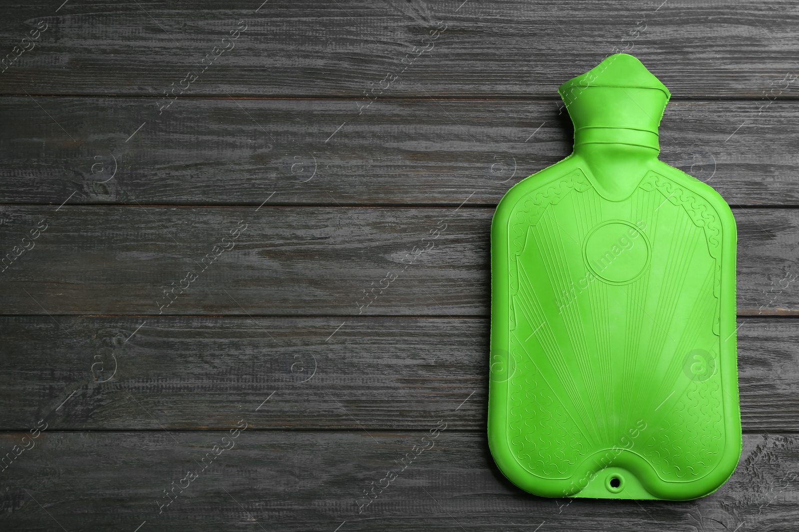 Photo of Green rubber hot water bottle on black wooden background, top view. Space for text