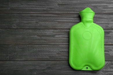 Photo of Green rubber hot water bottle on black wooden background, top view. Space for text