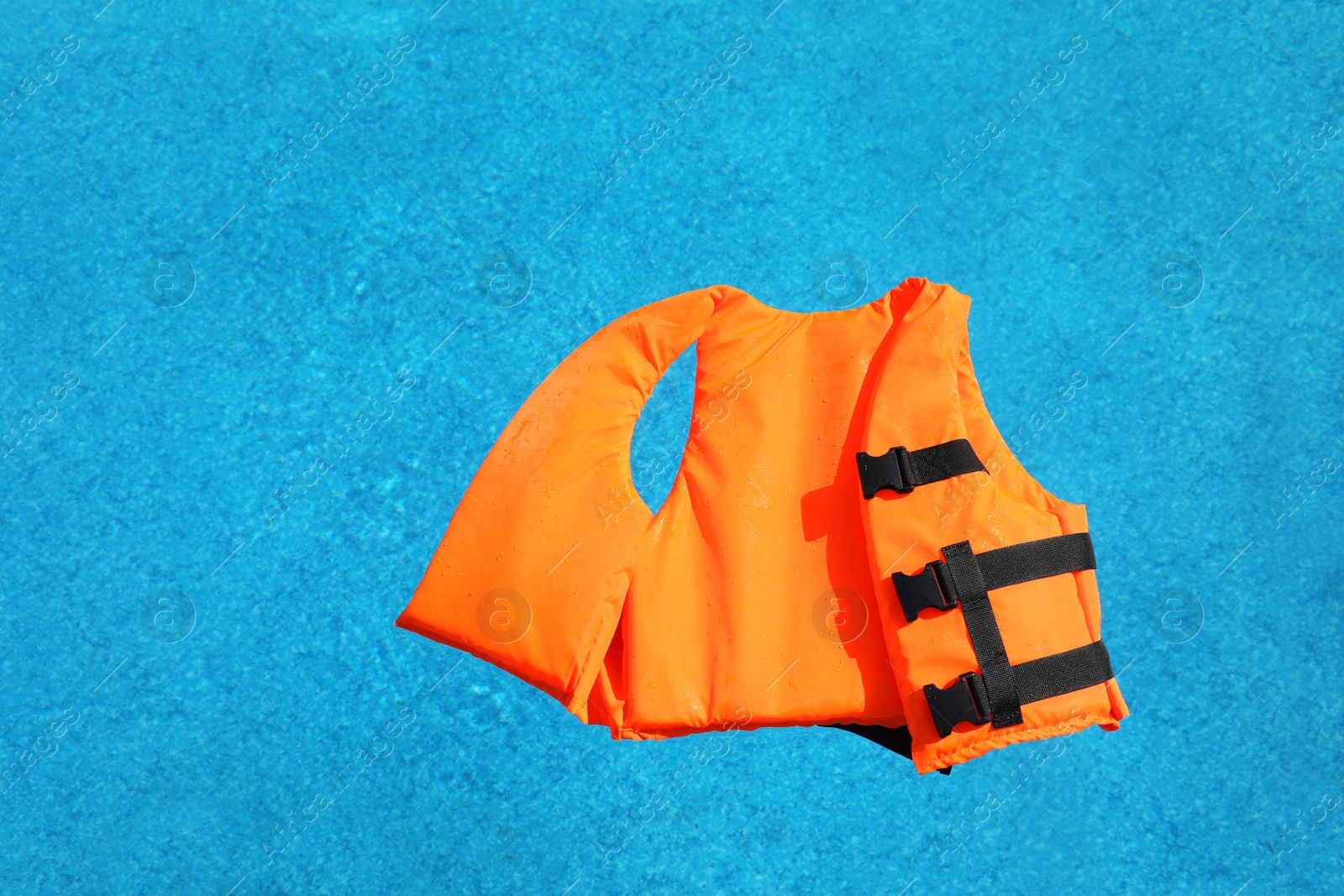 Bright orange life jacket floating in swimming pool, top view Photo of Bright orange life jacket floating in swimming pool, top view