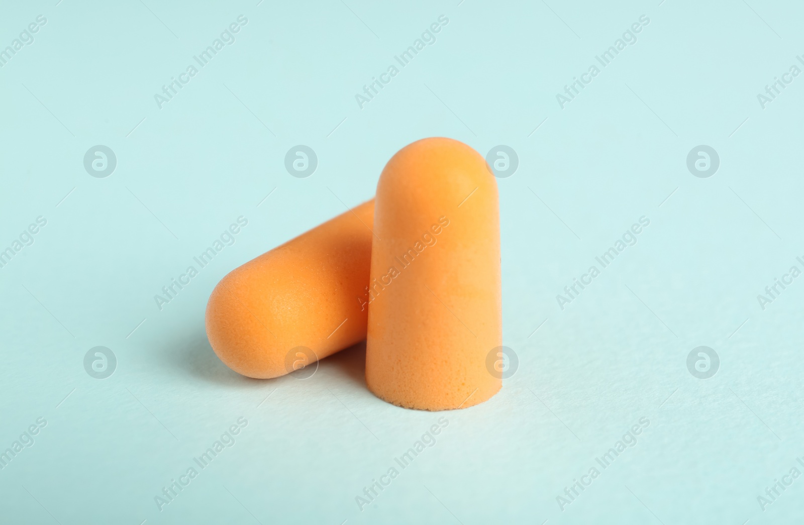 Pair of orange ear plugs on turquoise background Photo of Pair of orange ear plugs on turquoise background