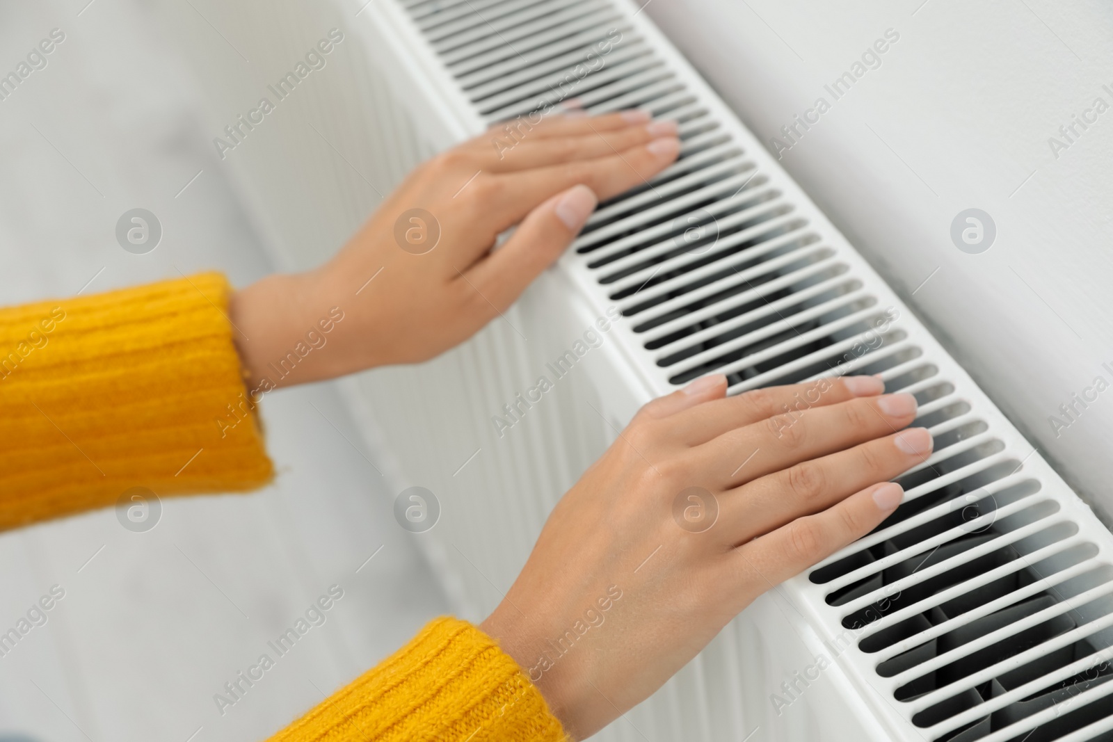Photo of Woman warming hands on heating radiator indoors, closeup