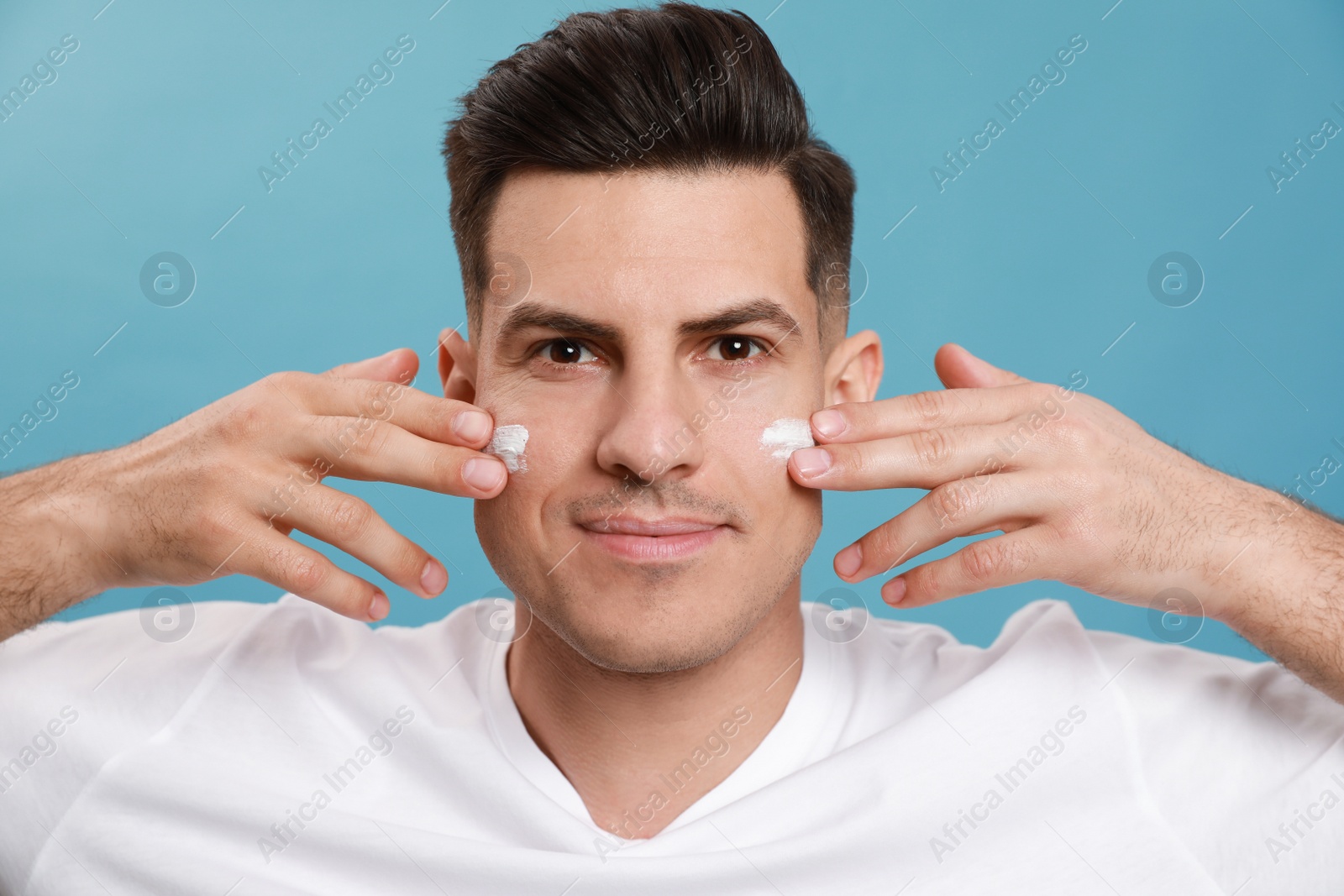 Handsome man applying face cream against turquoise background Photo of Handsome man applying face cream against turquoise background