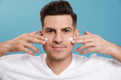 Handsome man applying face cream against turquoise background Photo of Handsome man applying face cream against turquoise background