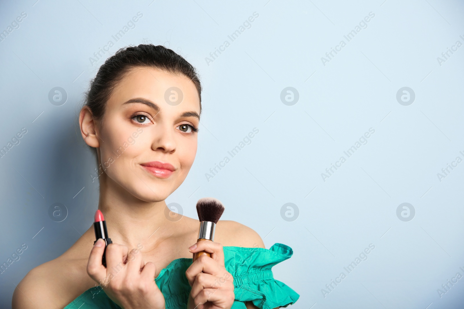 Young woman with lipstick and makeup brush on color background. Professional cosmetic products Photo of Young woman with lipstick and makeup brush on color background. Professional cosmetic products