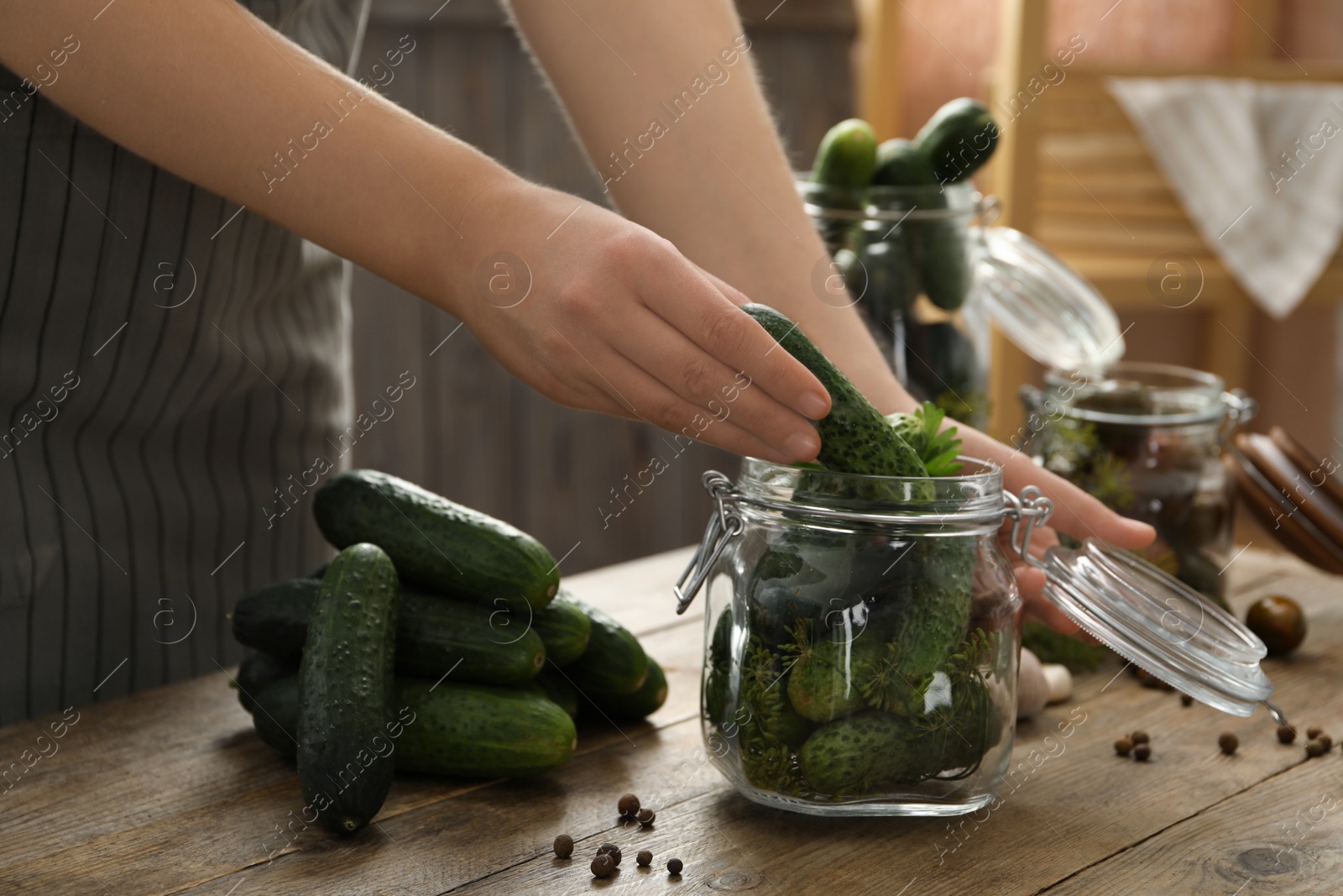 Woman putting cucumber into glass jar at wooden kitchen table, closeup. Pickling vegetables Photo of Woman putting cucumber into glass jar at wooden kitchen table, closeup. Pickling vegetables