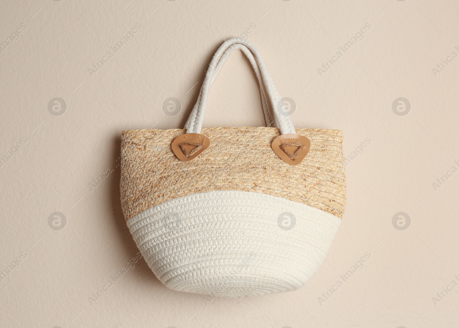 Elegant woman's straw bag hanging on beige background Photo of Elegant woman's straw bag hanging on beige background