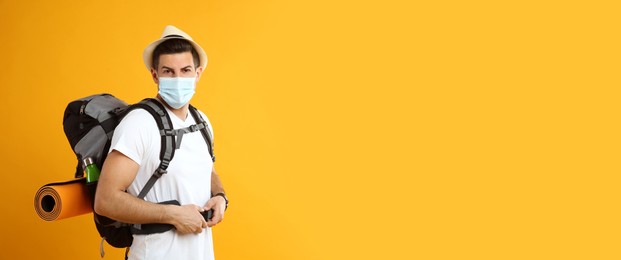 Male tourist in protective mask with travel backpack on yellow background, space for text Photo of Male tourist in protective mask with travel backpack on yellow background, space for text