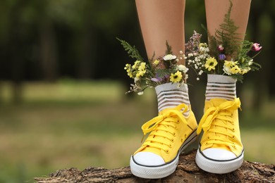 Woman standing on log with flowers in socks outdoors, closeup. Space for text Photo of Woman standing on log with flowers in socks outdoors, closeup. Space for text