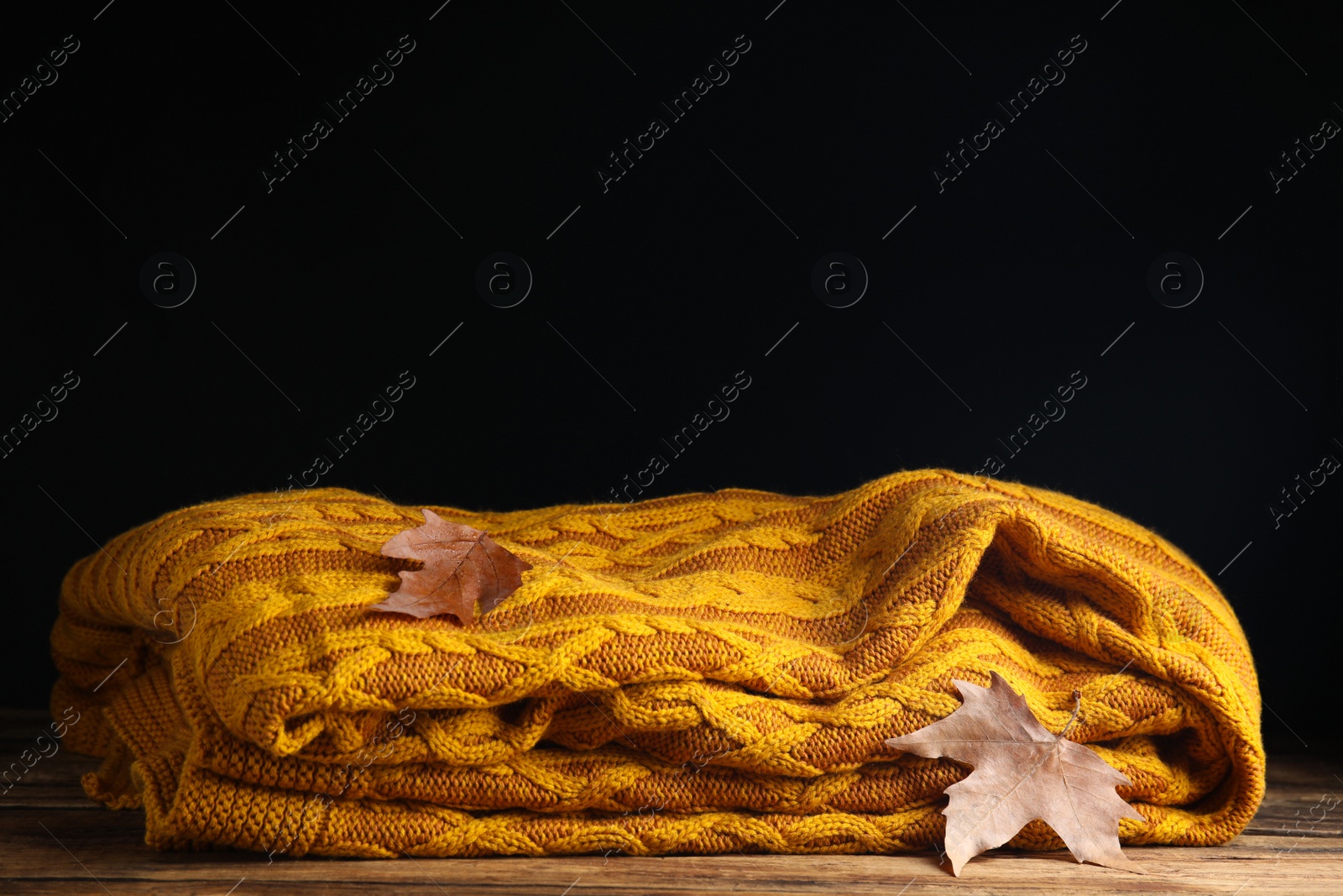 Orange knitted plaid with dry leaves on wooden table. Space for text Photo of Orange knitted plaid with dry leaves on wooden table. Space for text