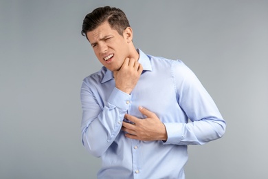 Photo of Young man suffering from sore throat on grey background