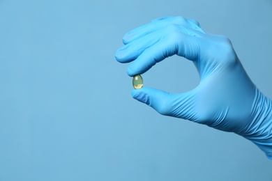 Scientist in protective gloves holding pill on light blue background, closeup. Space for text Photo of Scientist in protective gloves holding pill on light blue background, closeup. Space for text