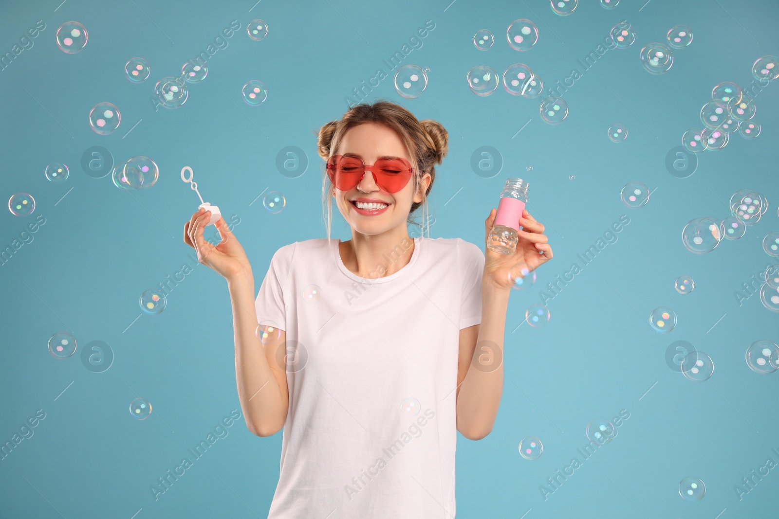 Young woman blowing soap bubbles on light blue background Photo of Young woman blowing soap bubbles on light blue background