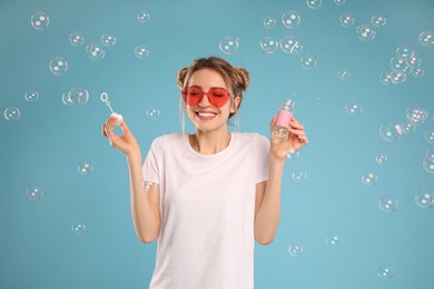 Young woman blowing soap bubbles on light blue background Photo of Young woman blowing soap bubbles on light blue background