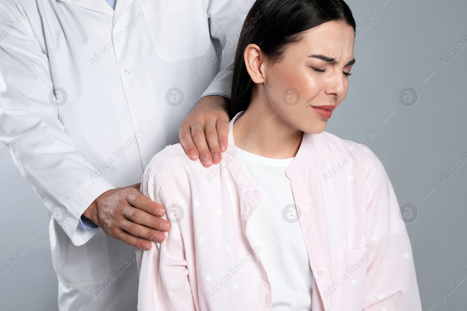 Photo of Doctor examining woman with shoulder pain on grey background
