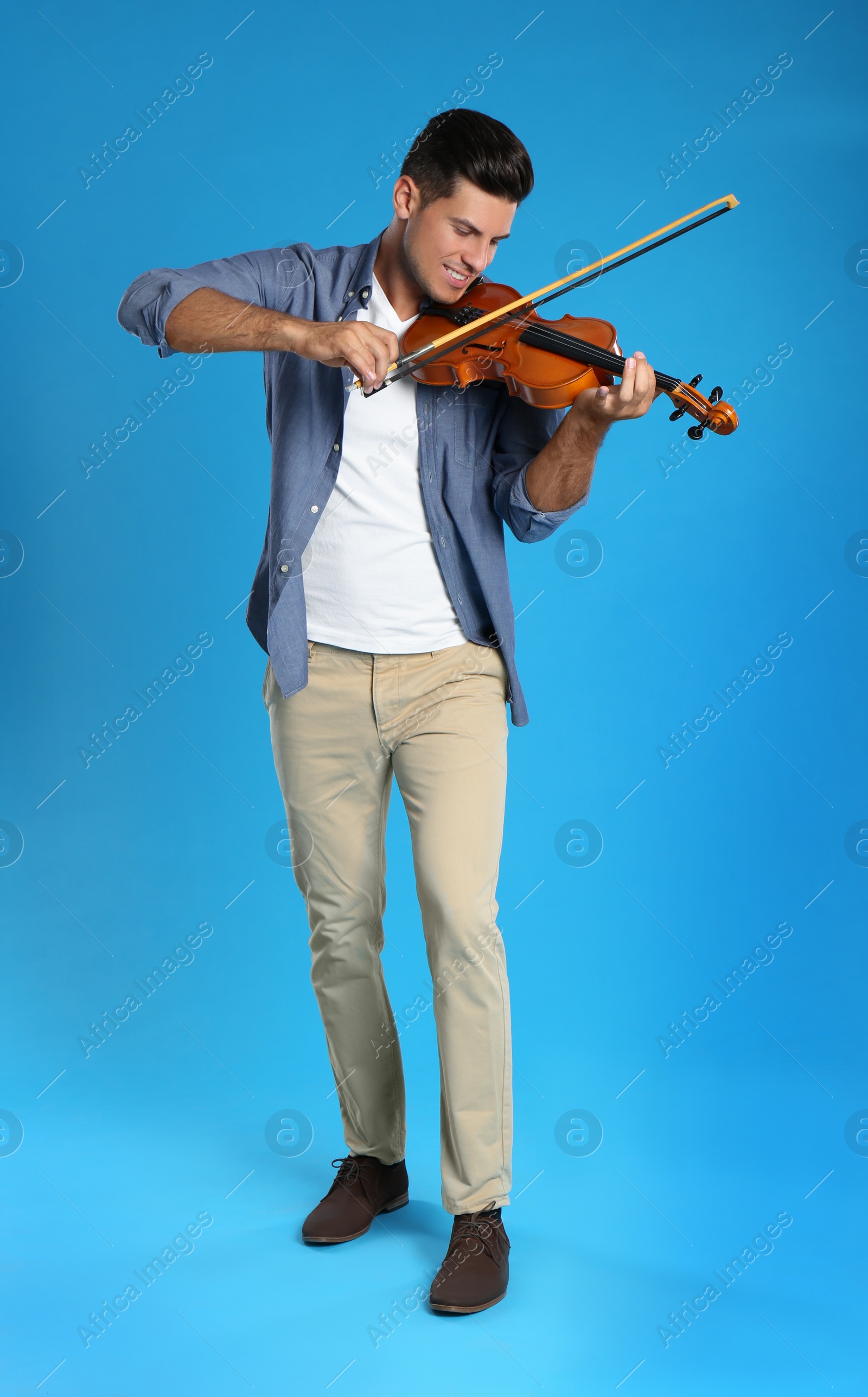Happy man playing violin on light blue background Photo of Happy man playing violin on light blue background