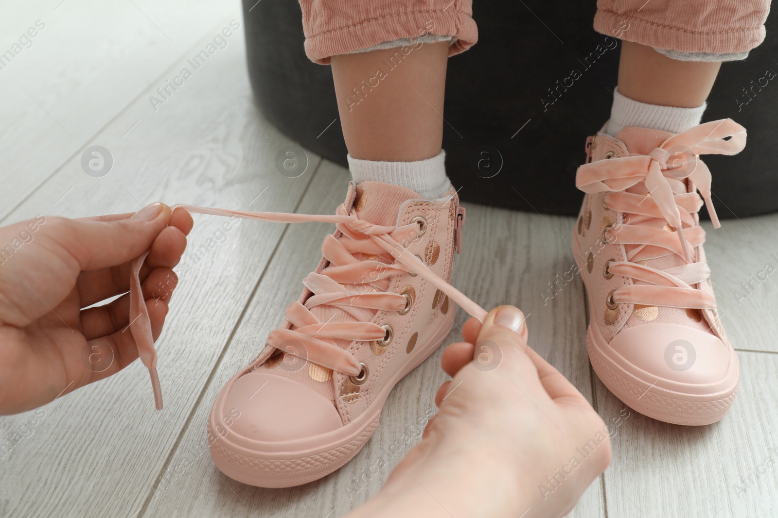 Mother helping daughter to tie shoe laces at home, closeup Photo of Mother helping daughter to tie shoe laces at home, closeup