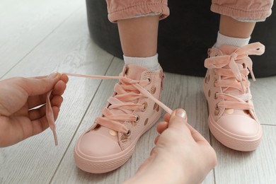 Mother helping daughter to tie shoe laces at home, closeup Photo of Mother helping daughter to tie shoe laces at home, closeup