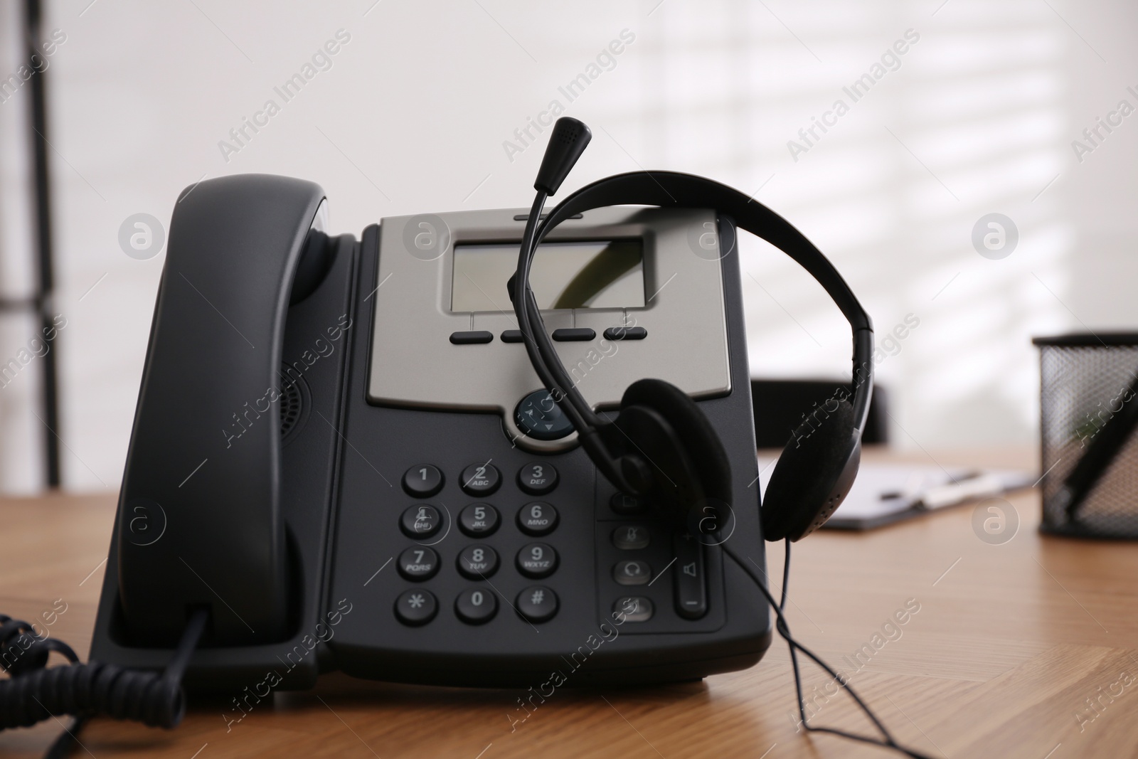 Desktop telephone and headset on wooden table in office. Hotline service Photo of Desktop telephone and headset on wooden table in office. Hotline service