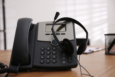 Desktop telephone and headset on wooden table in office. Hotline service Photo of Desktop telephone and headset on wooden table in office. Hotline service