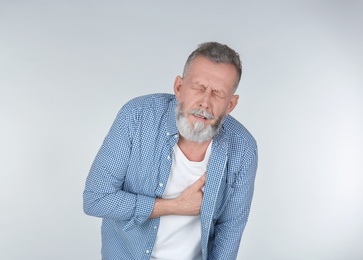 Man suffering from chest pain on light background Photo of Man suffering from chest pain on light background